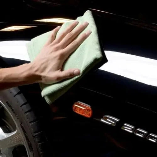 Hand using microfiber towel from Full Car Wash Kit Vonixx to polish a black car fender, enhancing shine and removing residue.